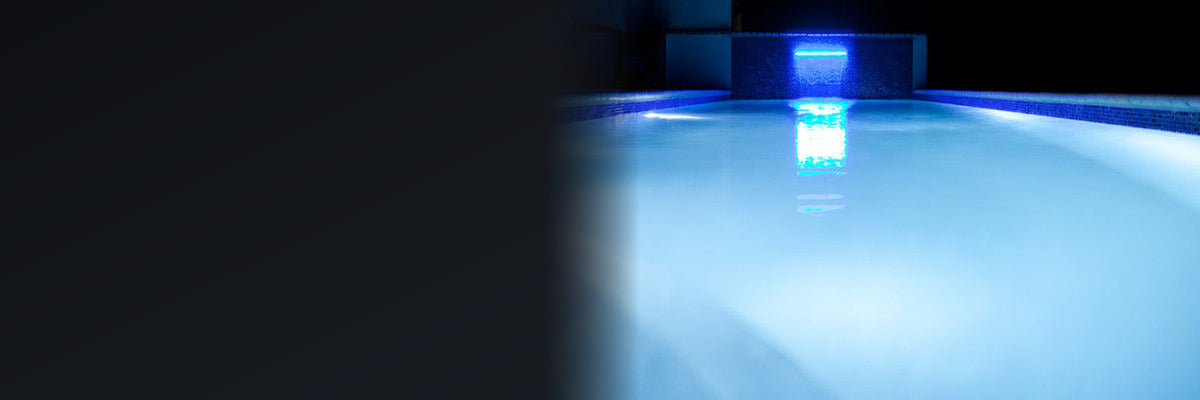 Swimming pool at night lit blue by LED pool lights, with a lit sheer descent waterfall